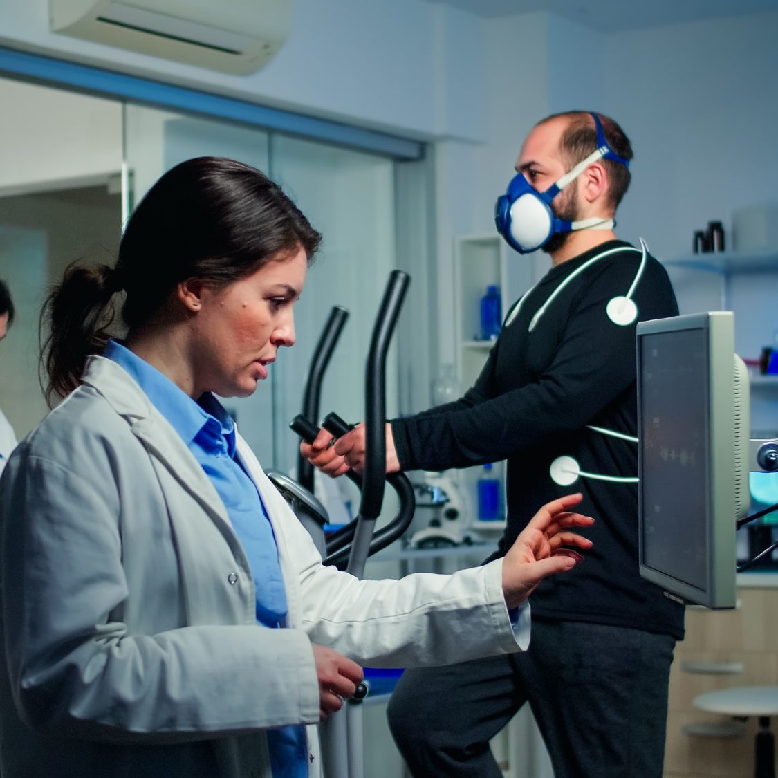 Doctor sport scientist checking EKG scan at monitor while man with mask running